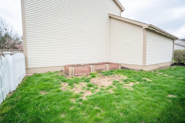 view of side of property with fence, a lawn, and a garden