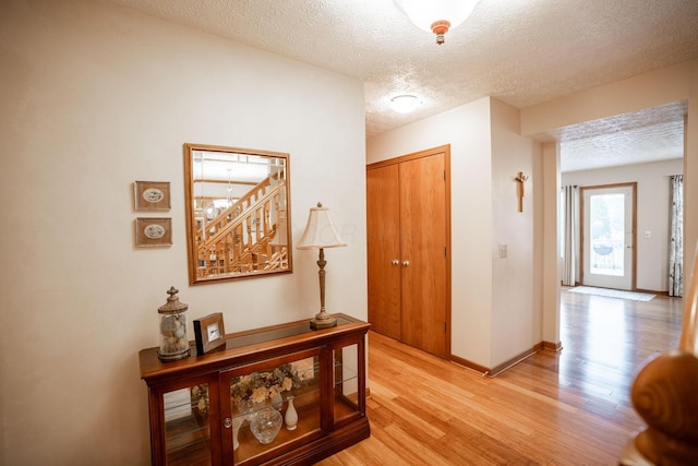corridor featuring baseboards, a textured ceiling, and light wood-style floors