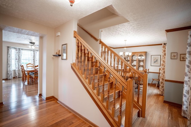 staircase featuring baseboards, wood finished floors, a textured ceiling, and ceiling fan with notable chandelier