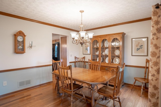 dining area featuring wood finished floors, visible vents, baseboards, a chandelier, and a textured ceiling