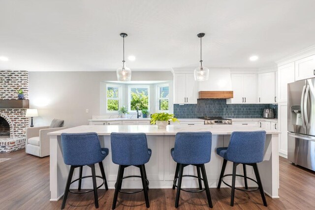 kitchen featuring a kitchen island, light countertops, stainless steel fridge with ice dispenser, white cabinets, and custom exhaust hood
