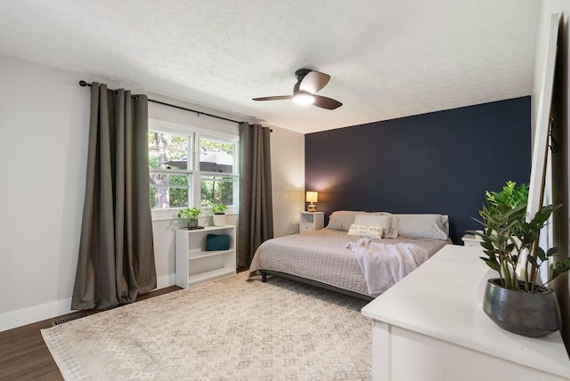 bedroom with baseboards, a textured ceiling, ceiling fan, and wood finished floors