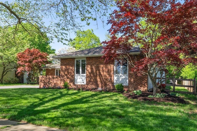 view of front of house featuring brick siding, a front lawn, and fence