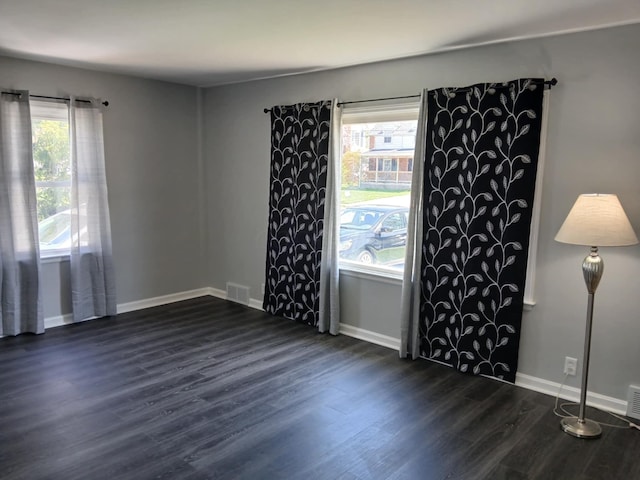 spare room with visible vents, baseboards, dark wood-style flooring, and a healthy amount of sunlight
