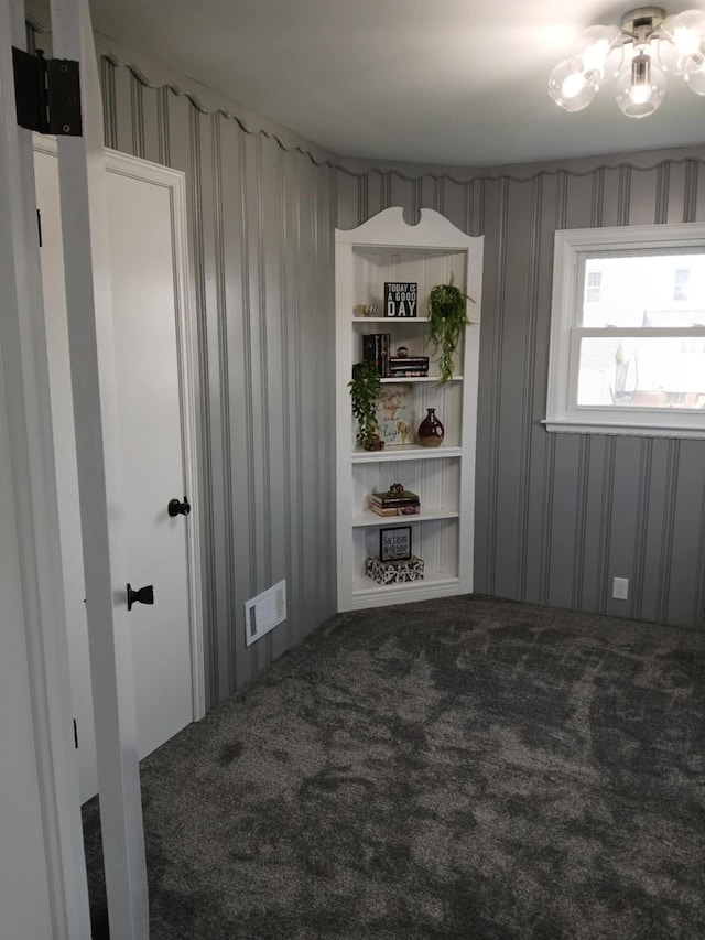 spare room featuring carpet floors, wallpapered walls, visible vents, and an inviting chandelier