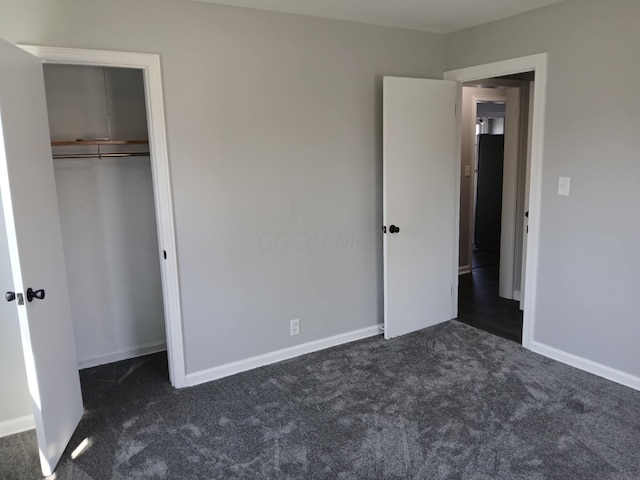 unfurnished bedroom with dark colored carpet, a closet, and baseboards