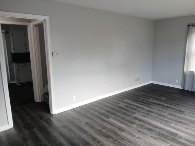 spare room with baseboards and dark wood-style floors