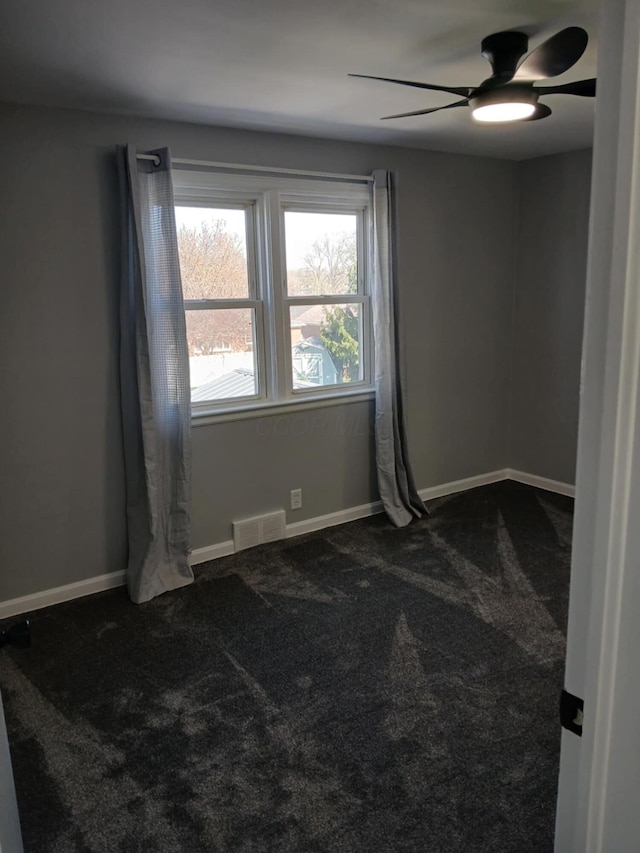 spare room featuring dark carpet, baseboards, a ceiling fan, and visible vents