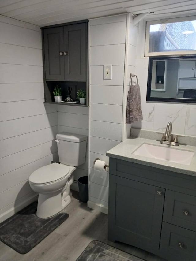 bathroom with toilet, vanity, wood finished floors, and wooden walls