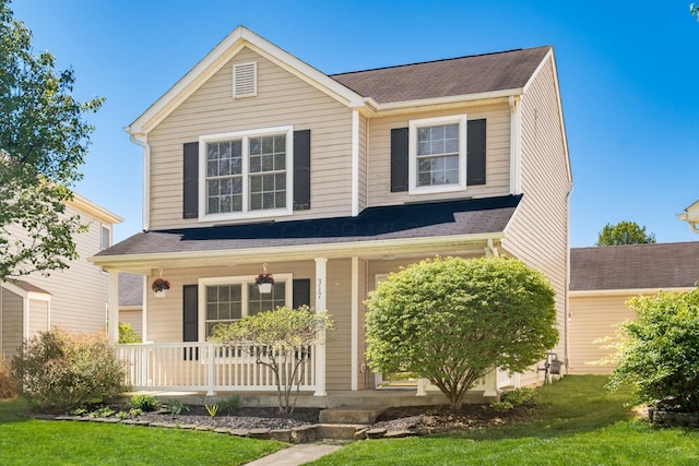 traditional-style home with covered porch, a shingled roof, and a front yard
