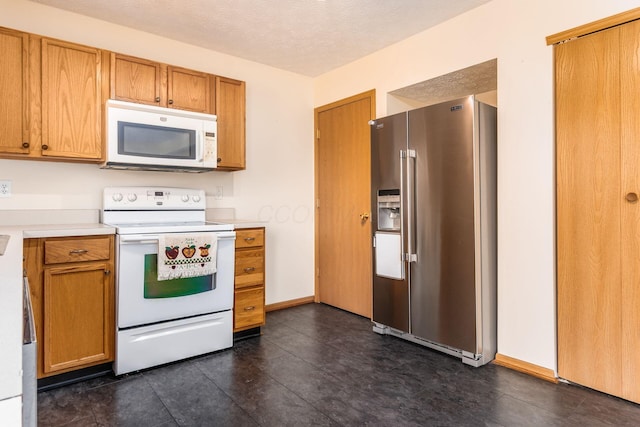 kitchen with brown cabinetry, a textured ceiling, light countertops, baseboards, and white appliances