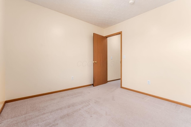 unfurnished room featuring baseboards, a textured ceiling, and light colored carpet