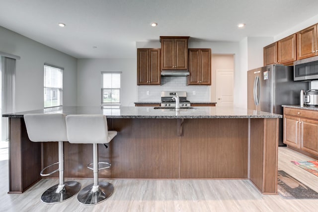 kitchen with light wood-style flooring, a sink, stainless steel microwave, dark stone counters, and backsplash