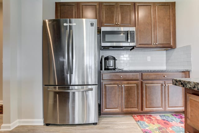 kitchen featuring light wood-style flooring, appliances with stainless steel finishes, decorative backsplash, and dark stone countertops