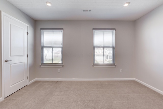 empty room featuring baseboards, visible vents, a wealth of natural light, and light carpet