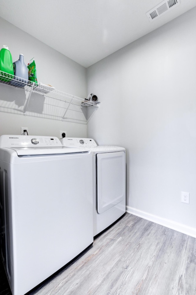 laundry room with washing machine and clothes dryer, baseboards, visible vents, light wood-style floors, and laundry area