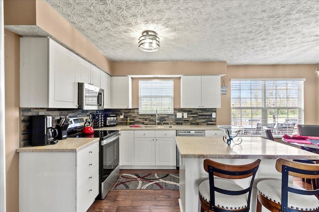 kitchen with a breakfast bar area, a sink, stainless steel appliances, light countertops, and dark wood-style floors