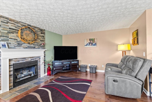 living room featuring baseboards, a stone fireplace, a textured ceiling, and wood finished floors