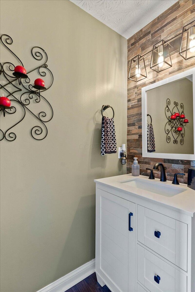 bathroom with vanity, wood walls, a textured ceiling, and baseboards