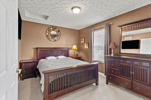 bedroom featuring a textured ceiling, attic access, visible vents, light carpet, and baseboards