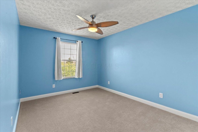 carpeted spare room featuring a textured ceiling, visible vents, baseboards, and ceiling fan