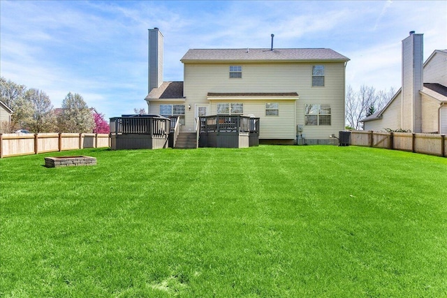 rear view of property with a fenced backyard, a wooden deck, a fire pit, and a yard
