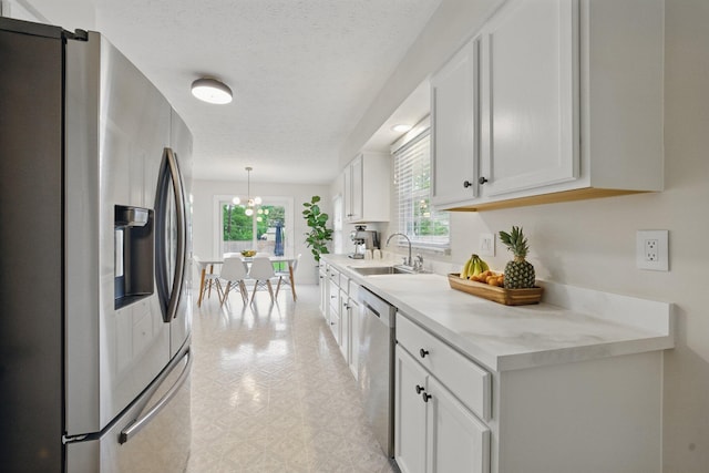 kitchen featuring stainless steel appliances, a sink, light countertops, white cabinetry, and decorative light fixtures