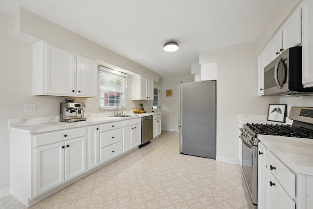 kitchen with appliances with stainless steel finishes, a sink, baseboards, white cabinets, and light flooring