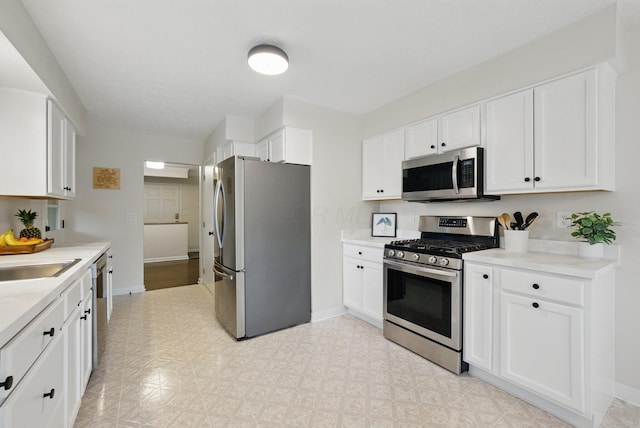 kitchen featuring appliances with stainless steel finishes, white cabinetry, light countertops, baseboards, and a sink