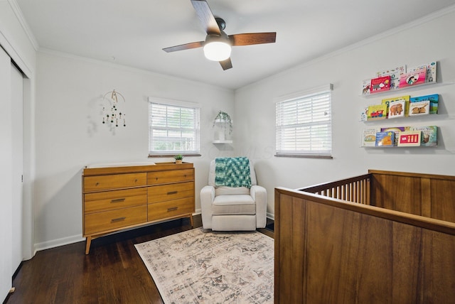 bedroom featuring dark wood-style floors, a nursery area, ornamental molding, a closet, and a ceiling fan