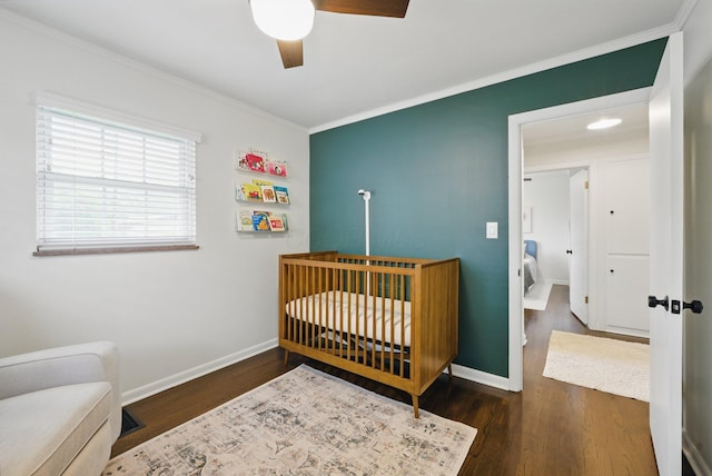 bedroom featuring crown molding, wood finished floors, a crib, baseboards, and ceiling fan
