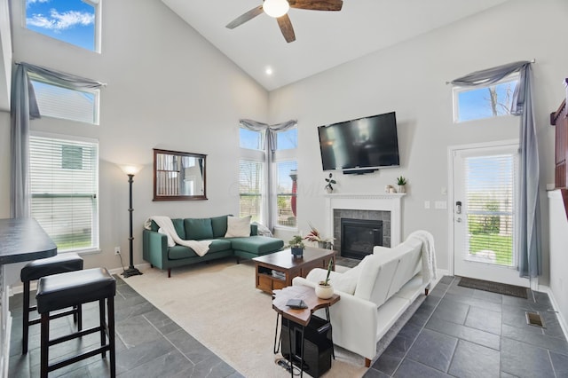living area with high vaulted ceiling, a wealth of natural light, a ceiling fan, and a tiled fireplace