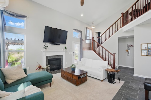 living room featuring a tiled fireplace, baseboards, a towering ceiling, stairs, and ceiling fan