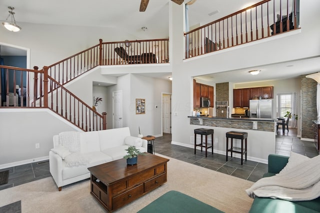 living room featuring stone tile flooring, baseboards, stairs, and ceiling fan