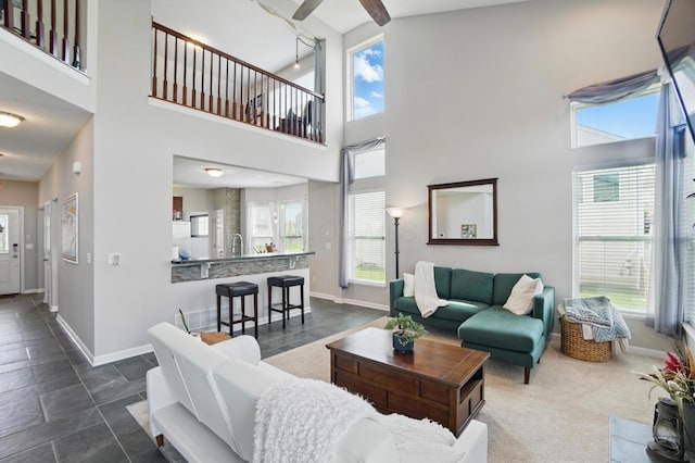 living area featuring a towering ceiling, a ceiling fan, and baseboards