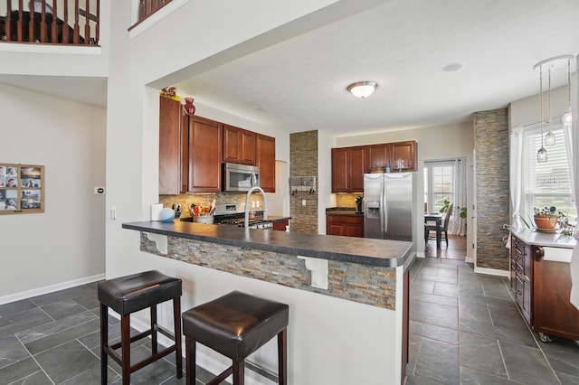 kitchen with dark countertops, a breakfast bar area, backsplash, a peninsula, and appliances with stainless steel finishes