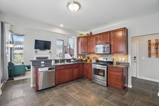 kitchen featuring dark countertops, a sink, open floor plan, stainless steel appliances, and a peninsula