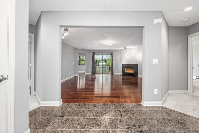 unfurnished living room with baseboards, a textured ceiling, and a glass covered fireplace
