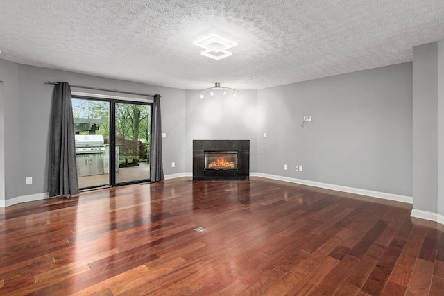 unfurnished living room featuring a textured ceiling, a multi sided fireplace, wood finished floors, and baseboards