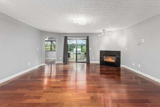 unfurnished living room with a fireplace with flush hearth, a textured ceiling, wood finished floors, and baseboards