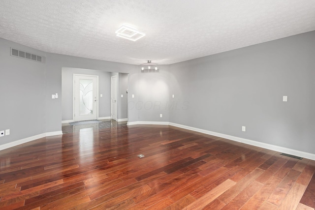 spare room with a textured ceiling, wood finished floors, visible vents, and baseboards