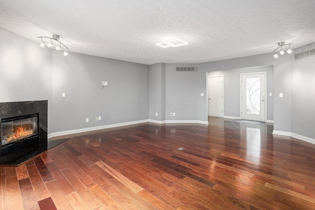 unfurnished living room with a textured ceiling, visible vents, a glass covered fireplace, and hardwood / wood-style floors