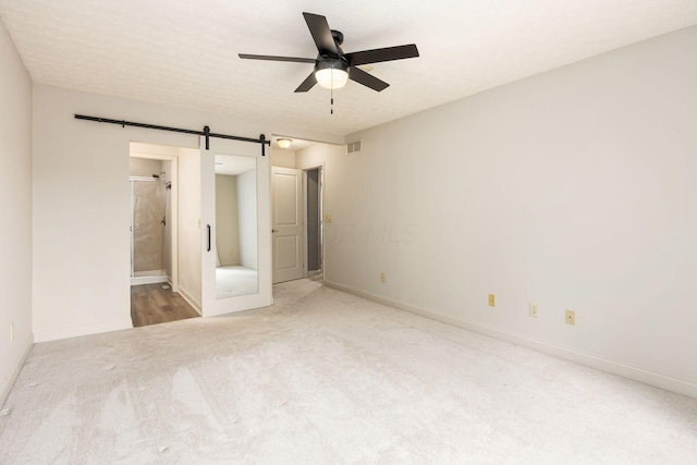 unfurnished bedroom featuring visible vents, baseboards, a barn door, and carpet floors