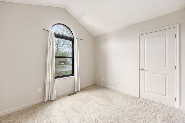 carpeted spare room with baseboards, visible vents, and vaulted ceiling