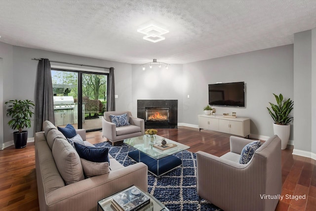 living area featuring a glass covered fireplace, wood finished floors, a textured ceiling, and baseboards