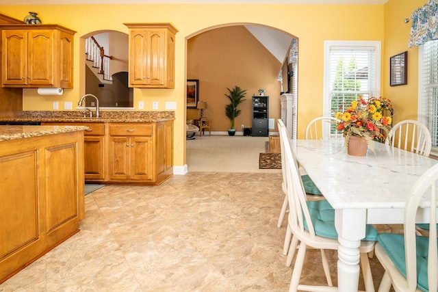 kitchen featuring light stone counters, arched walkways, brown cabinetry, and a sink