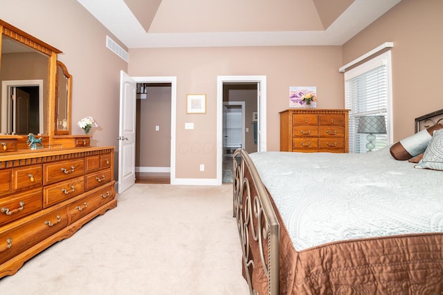 bedroom featuring visible vents, baseboards, a raised ceiling, light carpet, and ensuite bath