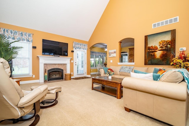 carpeted living area with high vaulted ceiling, visible vents, a fireplace with flush hearth, and a healthy amount of sunlight