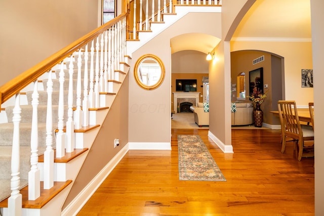 foyer featuring wood finished floors, a tile fireplace, visible vents, ornamental molding, and stairway