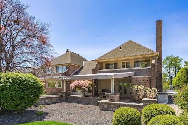 rear view of house featuring french doors, a chimney, central air condition unit, brick siding, and a shingled roof